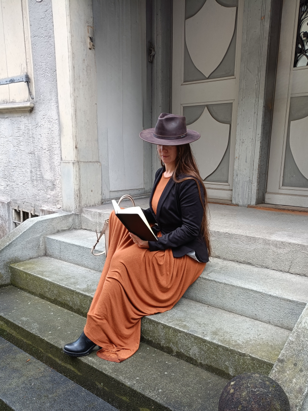 Andrea Egger – Business-Friendzone Expertin, sitzend auf Treppe mit Buch und Hut